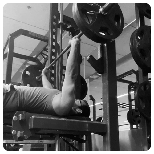 Black-and-white photo of Ali Lari bench pressing 225lbs (100kg).